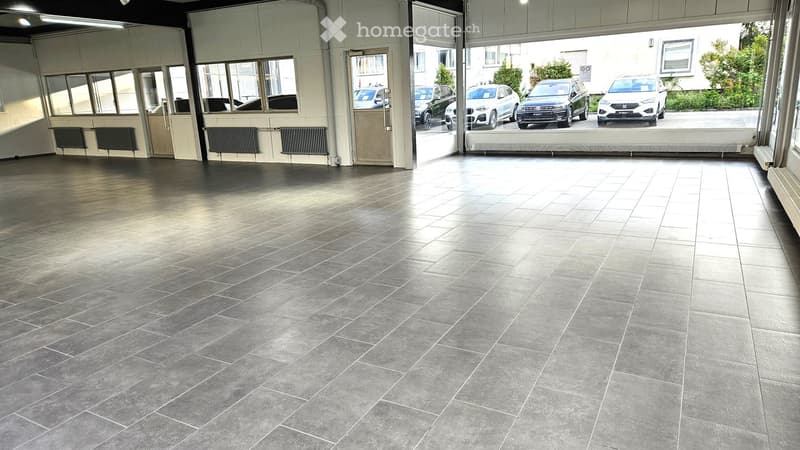 Empty garage with tiled floor, large windows, and a door leading outside. No furniture or equipment present.