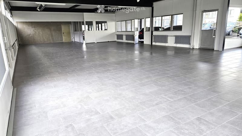 Empty room with grey tiled floor, white walls, large windows, and a door leading to an outdoor area.