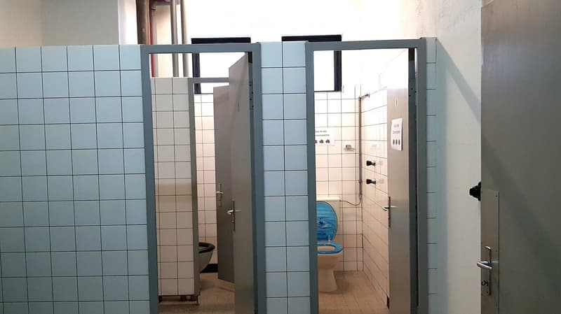 Public restroom with tiled walls, two stalls, and a toilet visible in one stall.