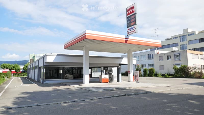 Gas station with a canopy, fuel pumps, and a small building. The sign reads "AVIA" and includes a car wash advertisement.
