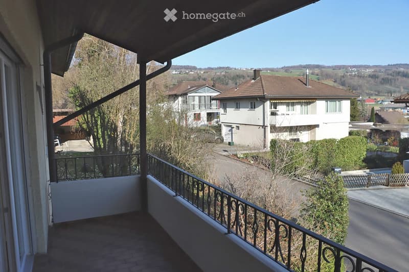 Balcony with metal railing overlooking a residential area with houses, trees, and a clear blue sky.