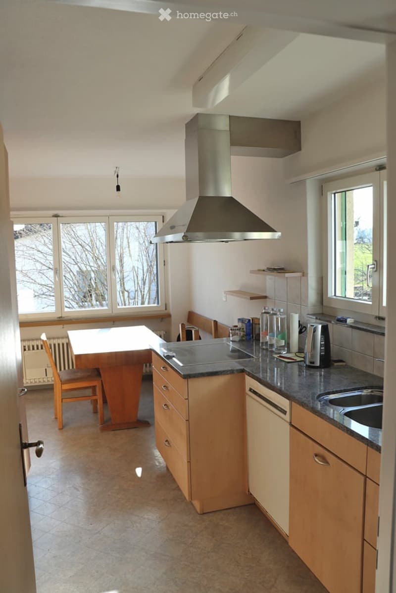 Bright kitchen with wooden cabinets, a central island, a dining table with chairs, and a modern stainless steel range hood.