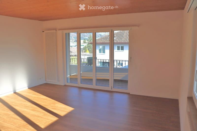 Empty room with wooden flooring, white walls, and large sliding glass doors leading to a balcony.
