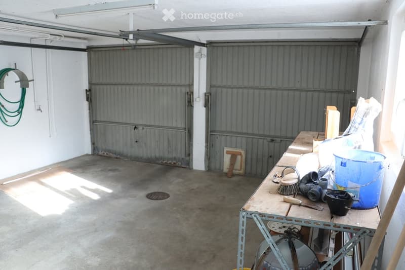 Empty garage with two large metal doors, a workbench with tools and supplies, and a concrete floor.