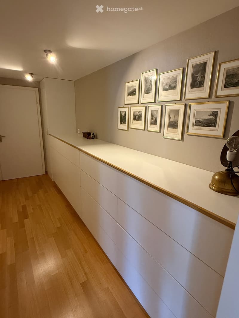 Hallway with light wooden flooring, white cabinetry, framed artwork on the wall, and a small decorative item on the cabinet.