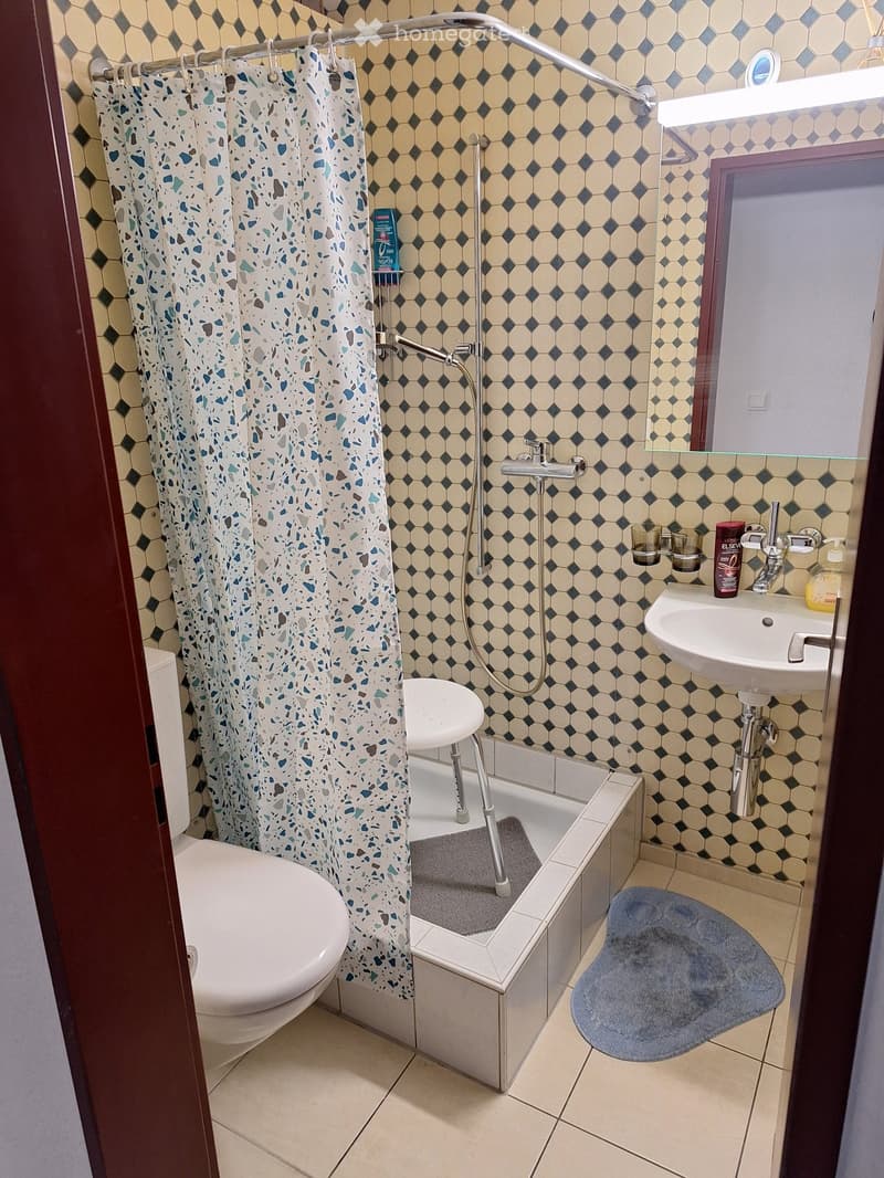 Bathroom with hexagonal tiles, toilet, bathtub with shower curtain, sink, and bath mat.