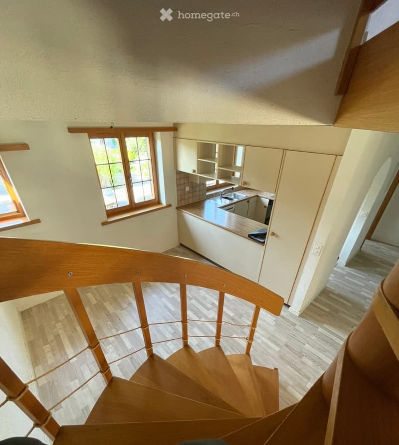 Spiral staircase leads down to a small kitchen area with light-colored cabinets, a countertop, and a sink.