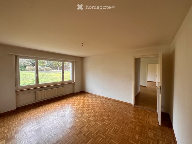 Empty room with wooden herringbone flooring, large windows, white walls, and a radiator. No furniture or equipment present.