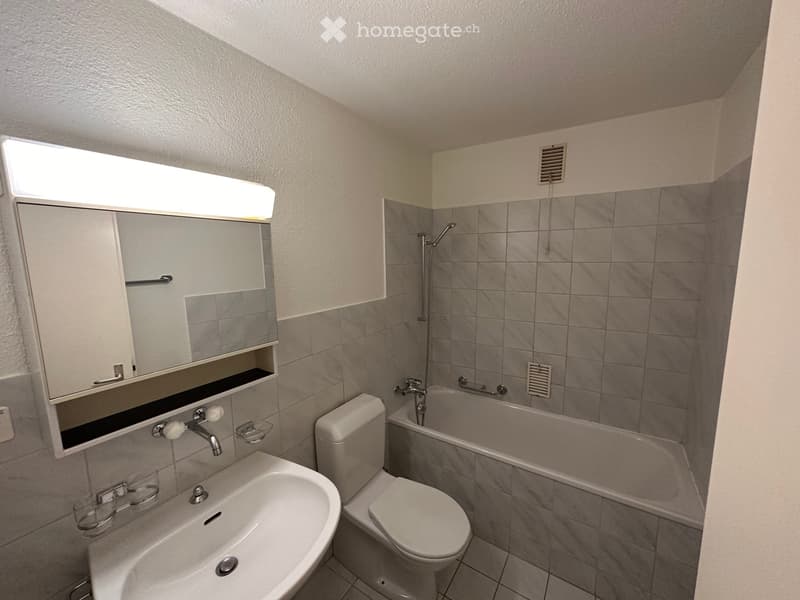 Modern bathroom with a white sink, toilet, bathtub, and a mirrored cabinet with built-in lighting above the sink.