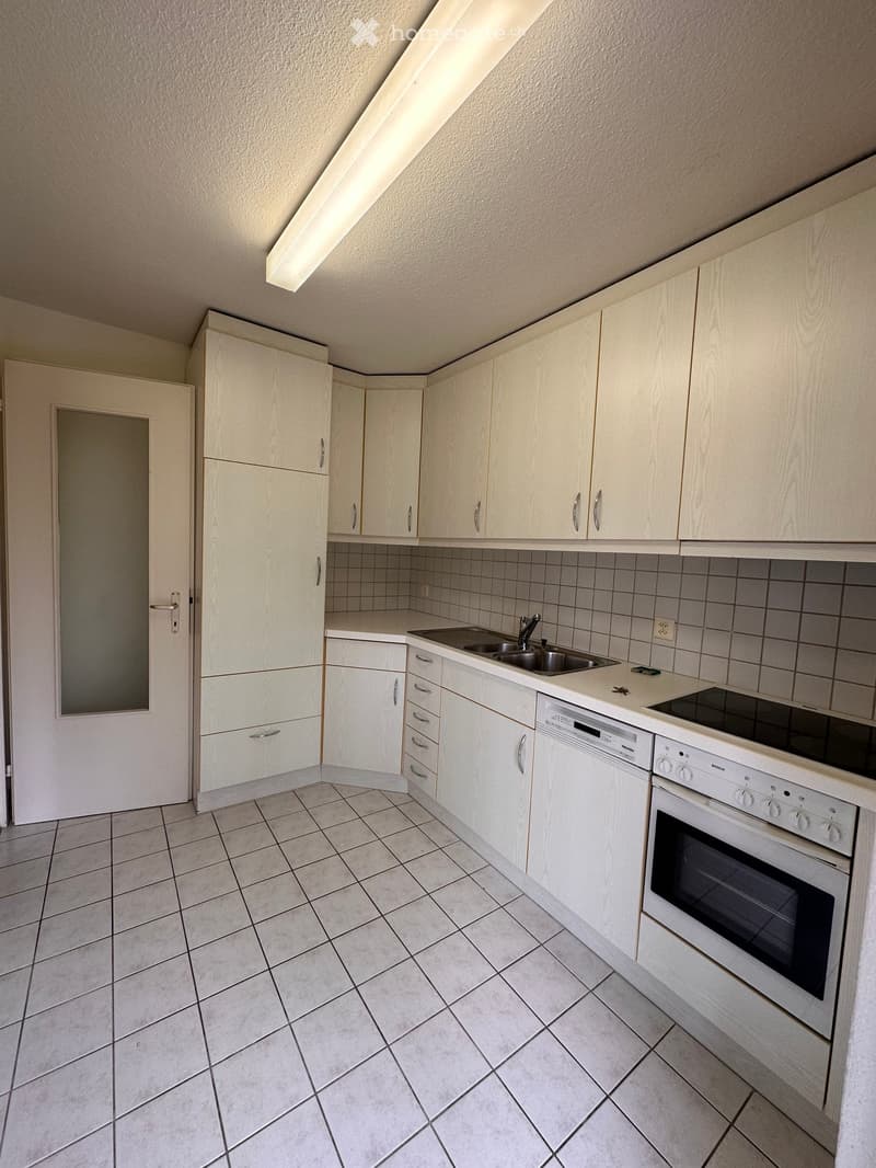 Modern kitchen with white cabinets, tiled floor, sink, oven, dishwasher, and built-in lighting.
