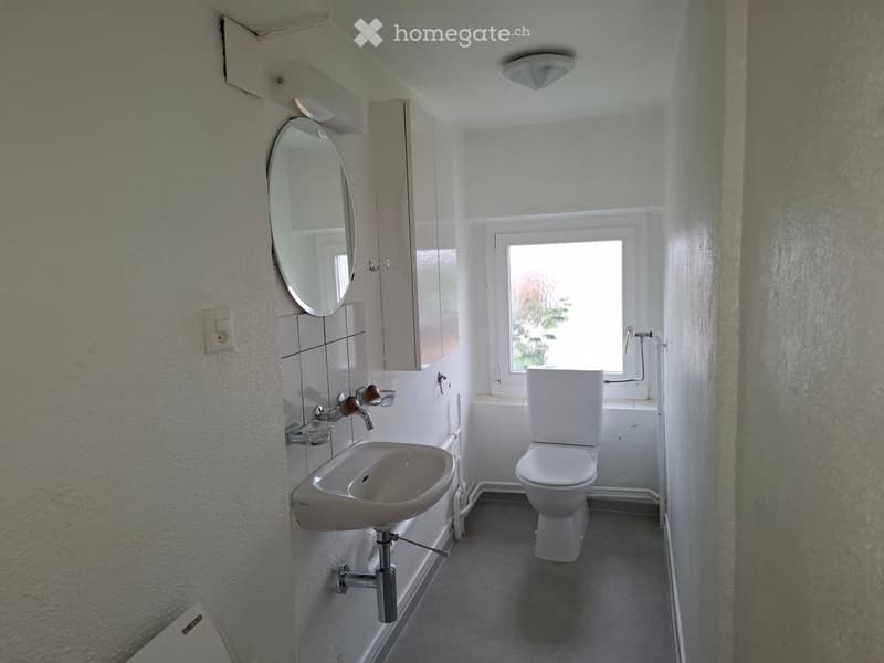Small bathroom with a white sink, toilet, mirror, and cabinet. The room has a window letting in natural light and is equipped with a modern faucet and storage space.