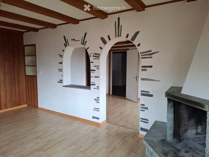 Empty hallway with wooden flooring, white walls, and a stone fireplace on the right side.