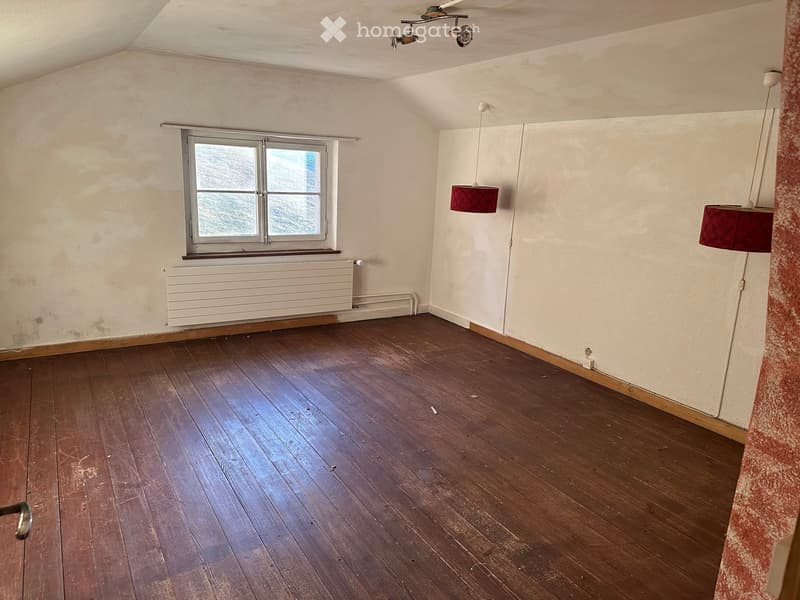 Empty room with wooden flooring, white walls, a window with a radiator below, and two hanging lamps with red shades.