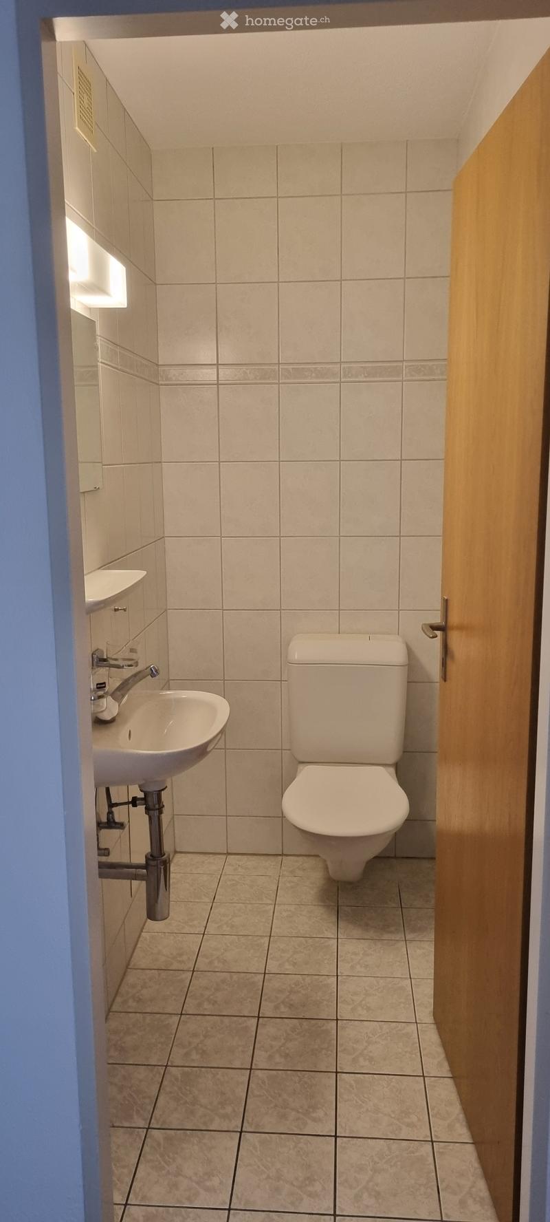 Small bathroom with beige tiled walls and floor, featuring a toilet and a sink with a chrome faucet.