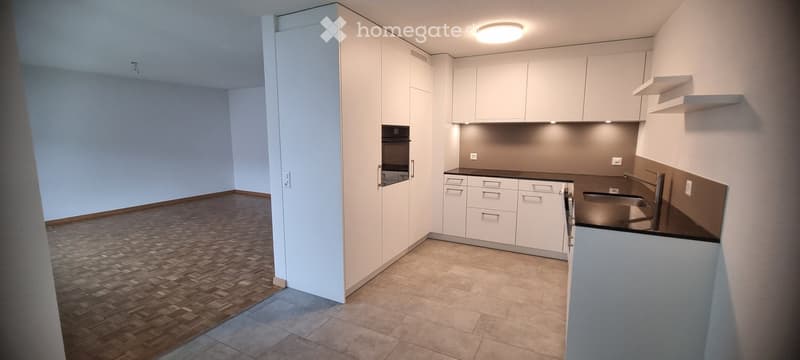 Modern kitchen with white cabinets, a dark countertop, and a built-in oven. The space features a combination of wooden and tiled flooring.