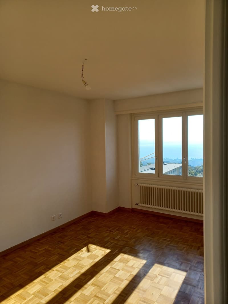 Empty room with wooden parquet flooring, white walls, and large windows offering a scenic view. No furniture or equipment is present.