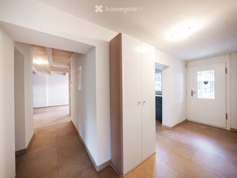 Bright hallway with tiled floor, white walls, built-in closet, and a door leading to another room.