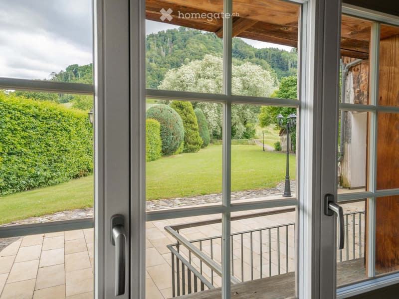 Balcony with wooden decking, metal railing, and scenic view of a green lawn, trees, and hills.