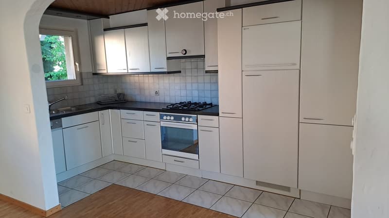 Modern kitchen with white cabinets, stainless steel appliances, and a black countertop. Features a sink, stove, and oven, with a window providing natural light.