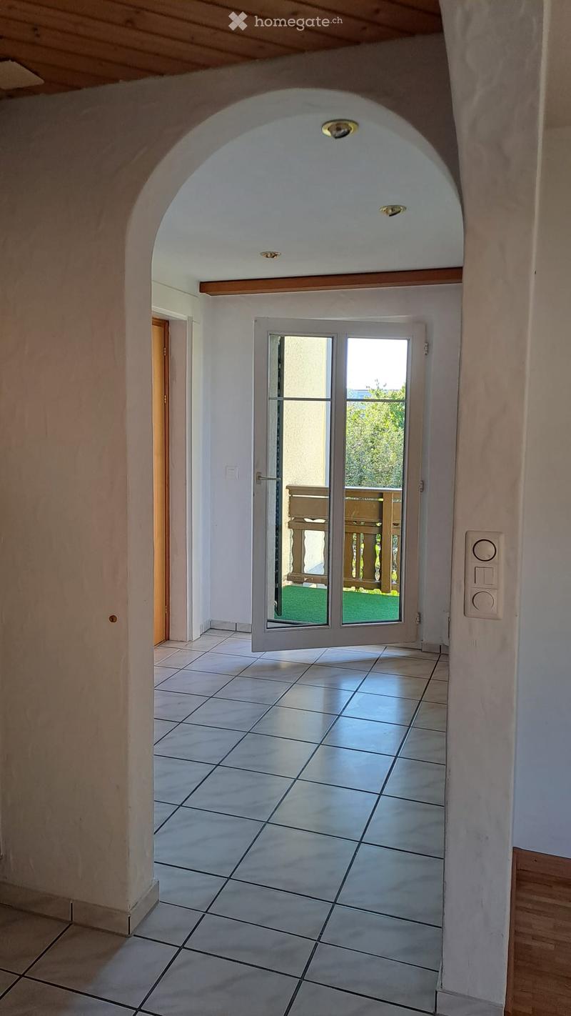 Hallway with tiled floor, arched ceiling, and a door leading to a balcony area with wooden railing and green outdoor space.