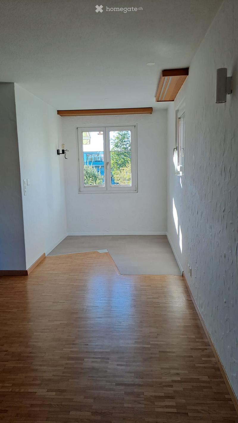 Empty hallway with wooden flooring, white walls, and a large window at the end. No furniture or equipment is present.