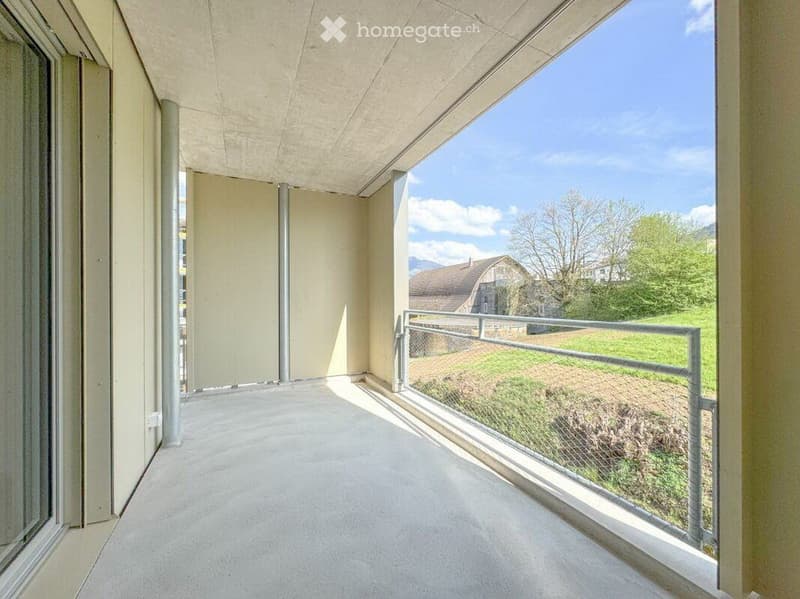 Modern balcony with concrete floor, glass sliding doors, metal railing, and scenic mountain view.