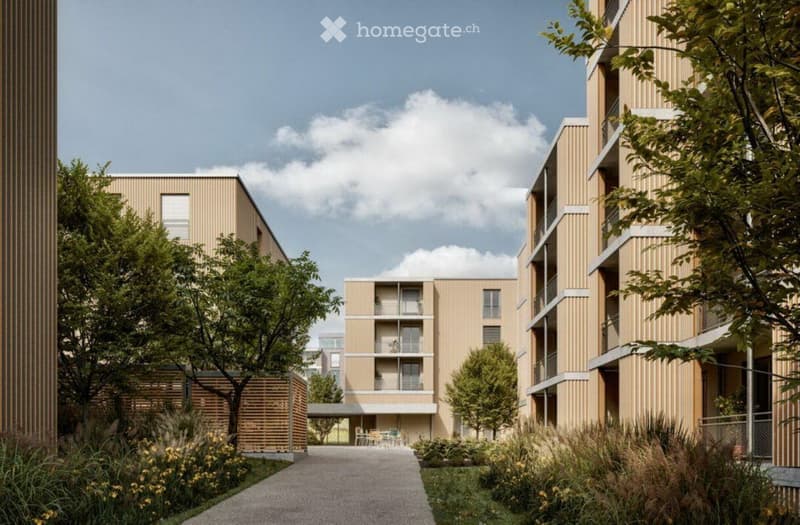 Modern multi-story residential building with beige facades, balconies, and surrounding greenery including trees and shrubs.