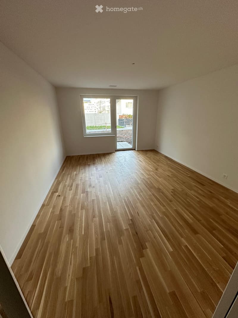 Empty room with wooden flooring and white walls, featuring a large window and a sliding glass door leading to an outdoor area.
