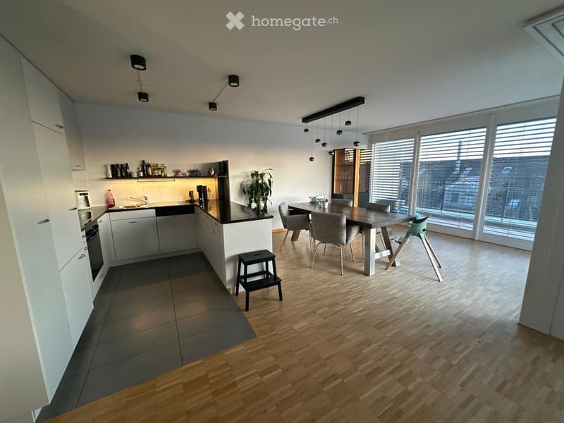 Modern kitchen with white cabinets, a central island, and a dining area. Features include a dishwasher, oven, sink, and a small table with chairs.