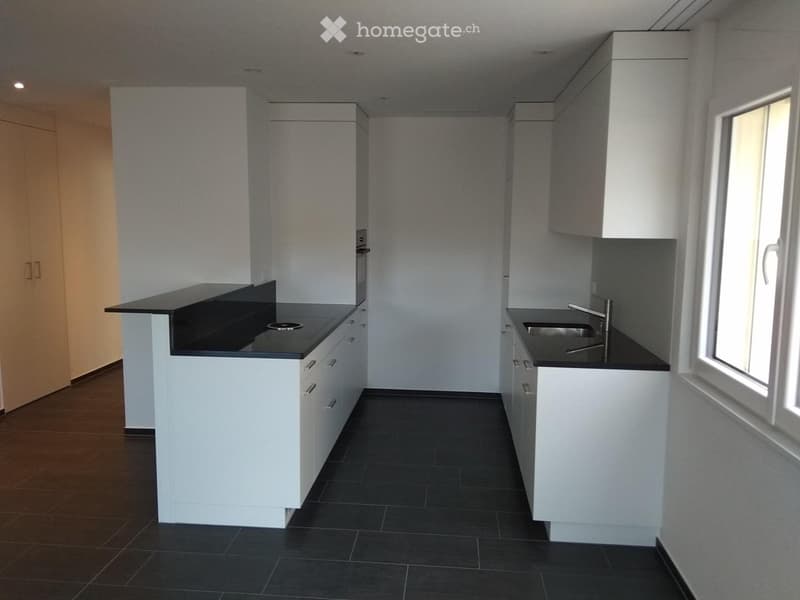 Modern kitchen with white cabinets, black countertops, and a stainless steel sink. The space features a central island with a built-in oven and ample storage.