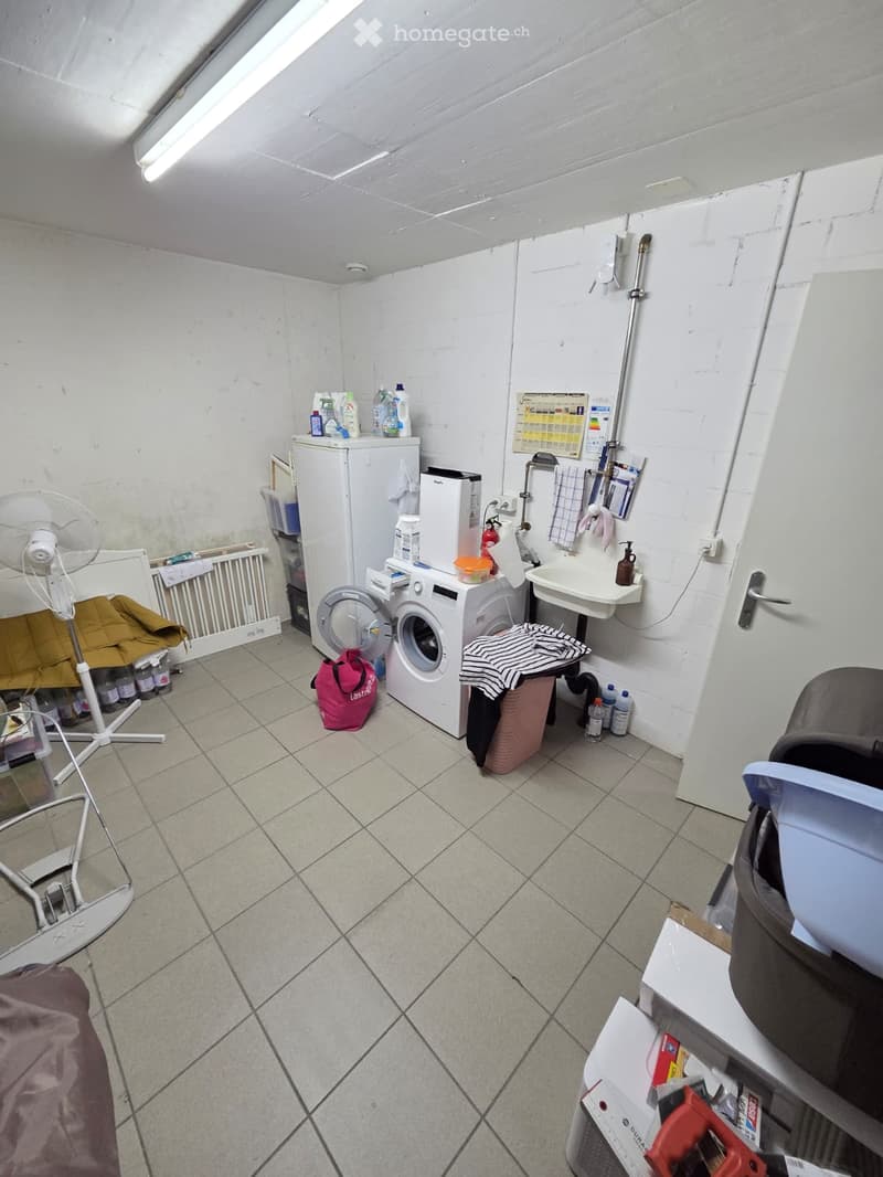 The room is a utility space with a washing machine, refrigerator, fan, sink, and various storage items.