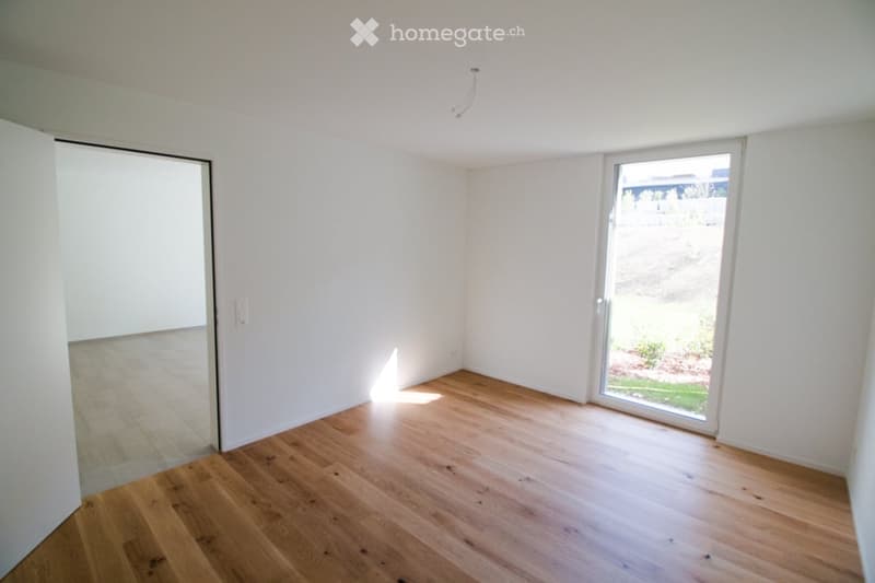 Empty room with wooden flooring, white walls, and a large sliding glass door leading to an outdoor area.