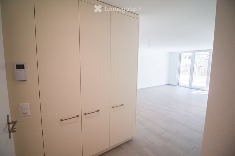Empty room with white walls, tiled floor, large sliding glass doors leading to an outdoor area, and built-in white closet with handles.