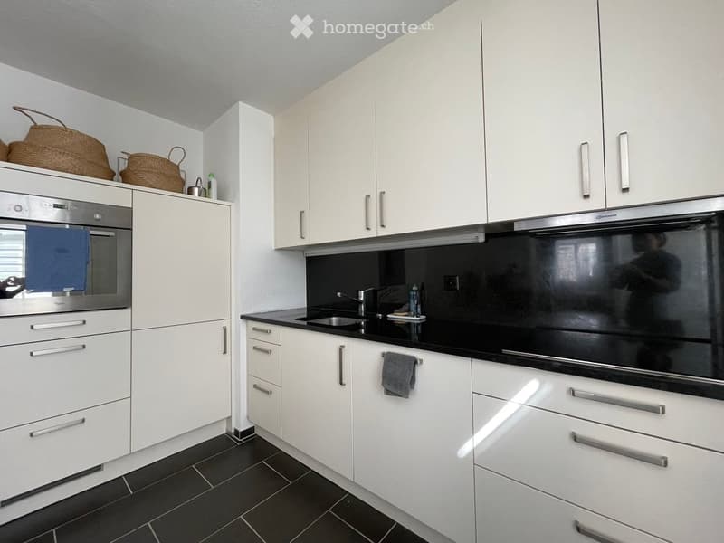 Modern kitchen with white cabinets, black countertops, stainless steel oven, sink, and faucet. Includes a wicker basket on top of the cabinets.