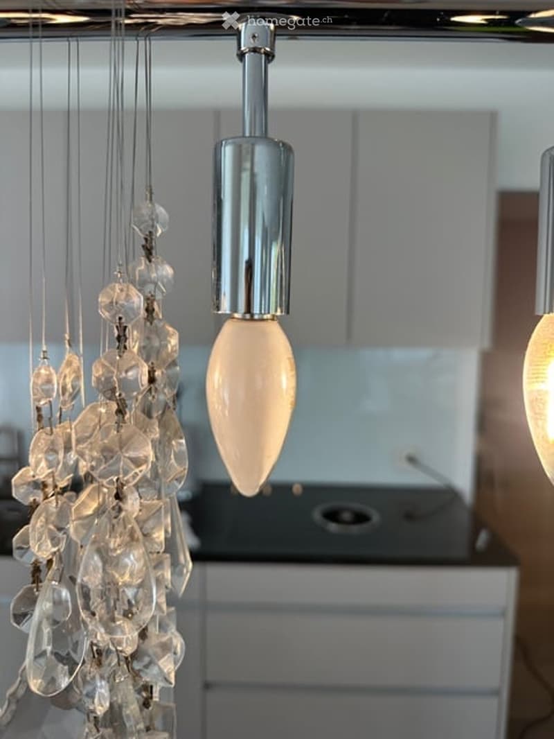 Modern kitchen with sleek white cabinets and a central island, illuminated by a stylish pendant light with a crystal-like glass shade.