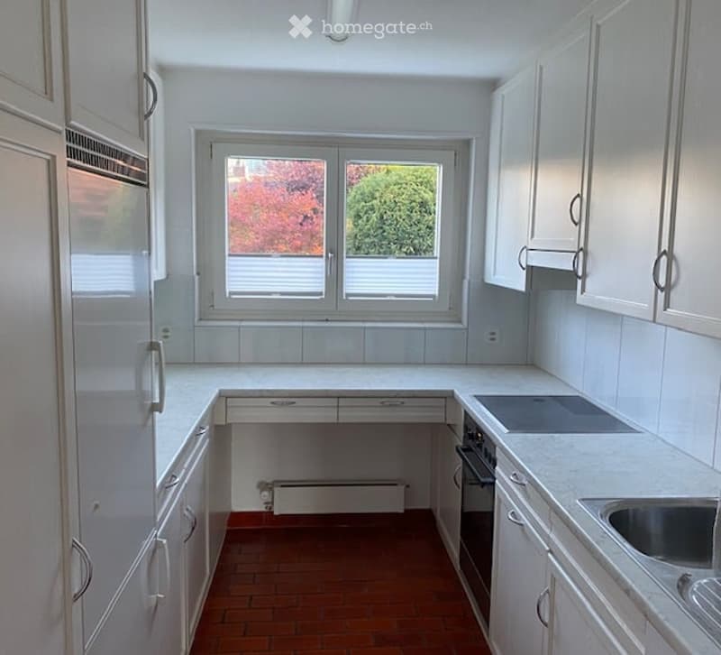 Bright kitchen with white cabinets, a central island, and a window overlooking a garden. Features include a sink, oven, and radiator under the window.