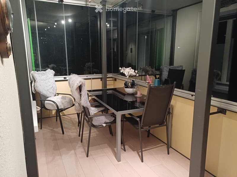 Balcony with tiled floor, glass table, two chairs with fur cushions, and a small flower pot.
