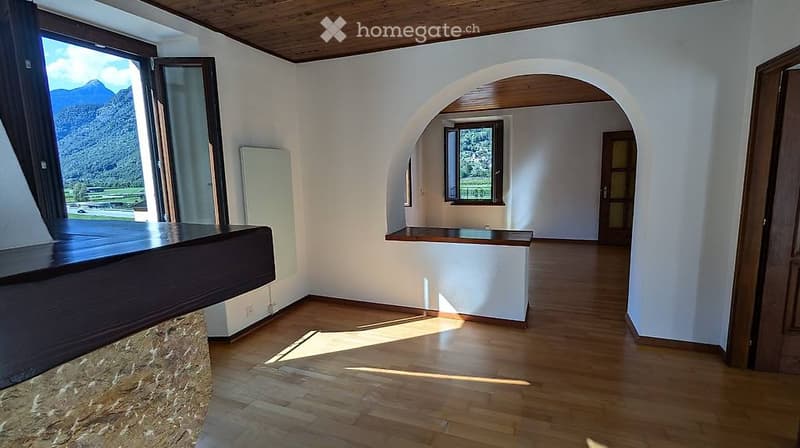 Empty room with wooden flooring, white walls, large windows offering a mountain view, and a small built-in bench.