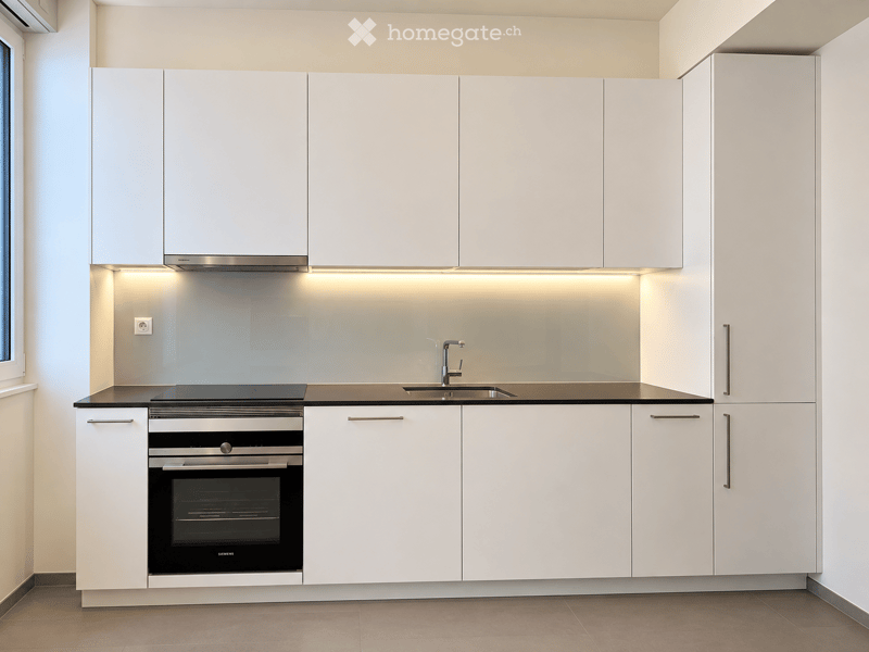 Modern kitchen with white cabinets, built-in oven, sink, and sleek countertops.