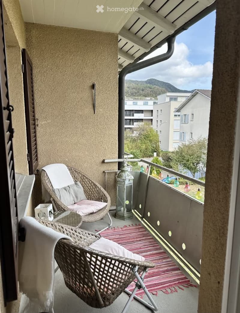 Balcony with a view of mountains, featuring two wicker chairs, a small table, and a lantern.