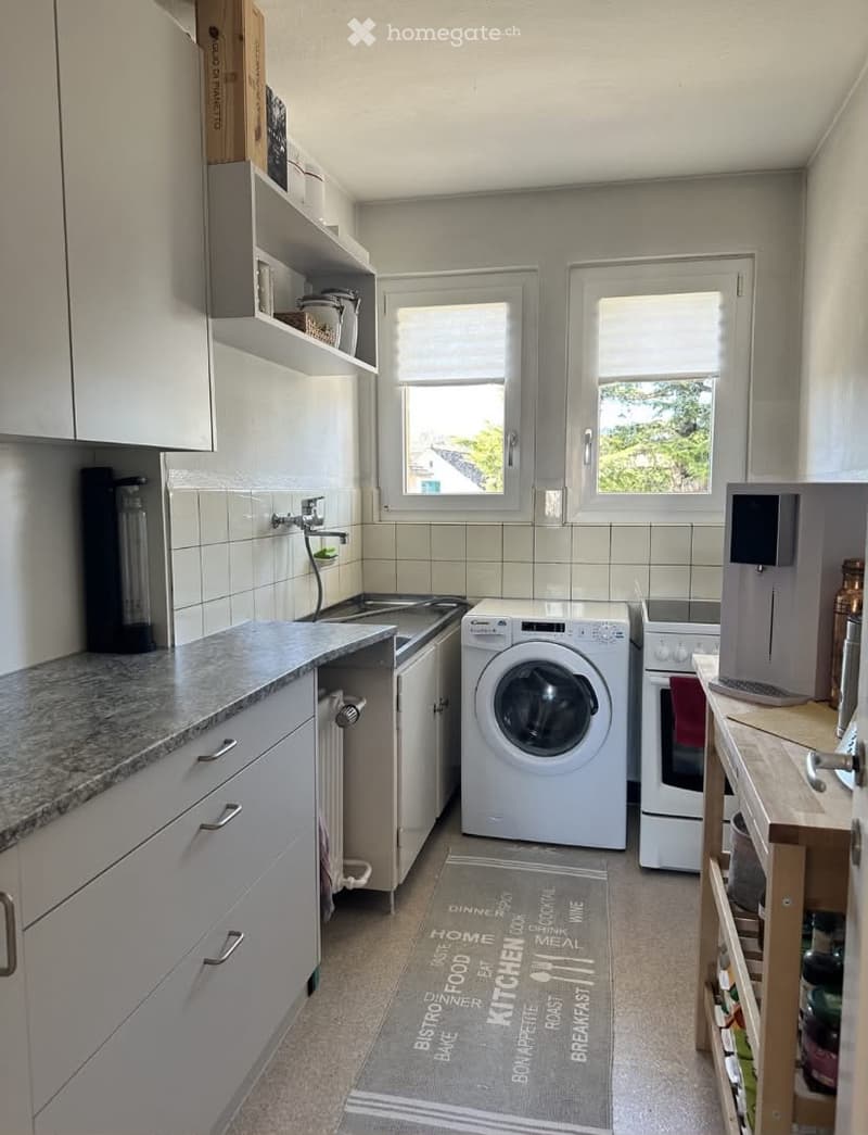 Modern kitchen with white cabinets, granite countertop, sink, washing machine, oven, coffee maker, and shelves.