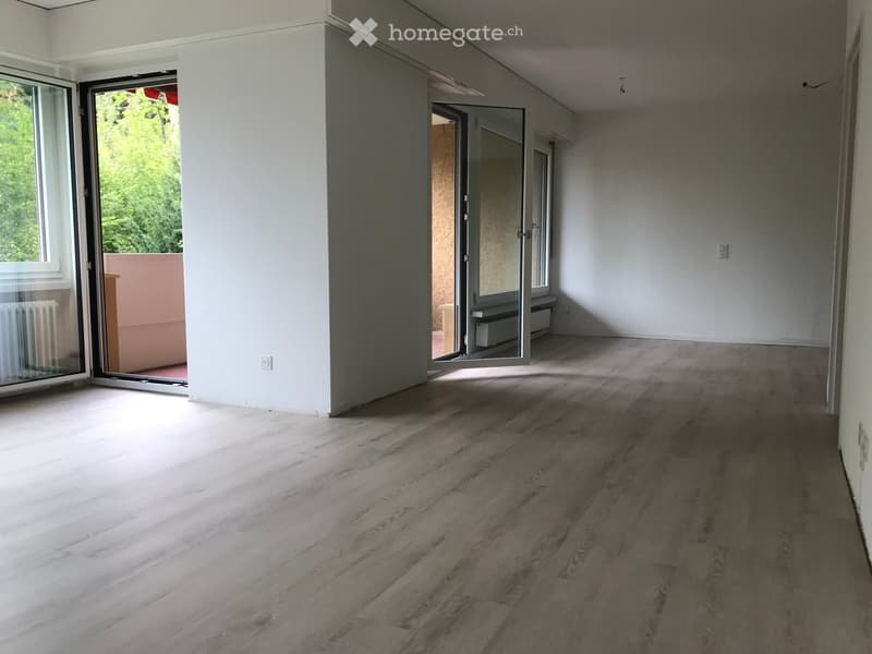 Empty room with wooden flooring, white walls, and large sliding glass doors leading to a balcony area.