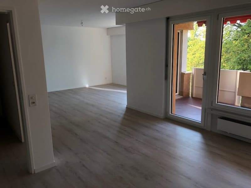 Empty room with wooden flooring, white walls, and a sliding glass door leading to a balcony.