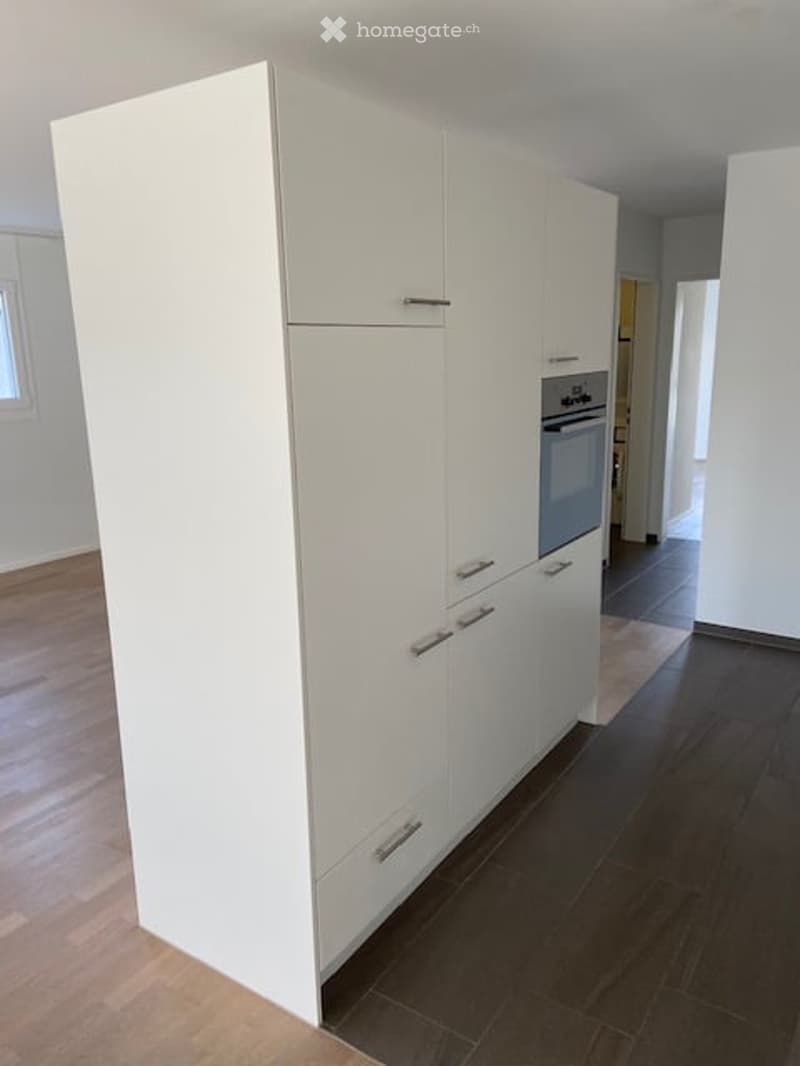 Modern kitchen with white cabinets and a built-in oven, featuring dark wooden flooring and light-colored walls.