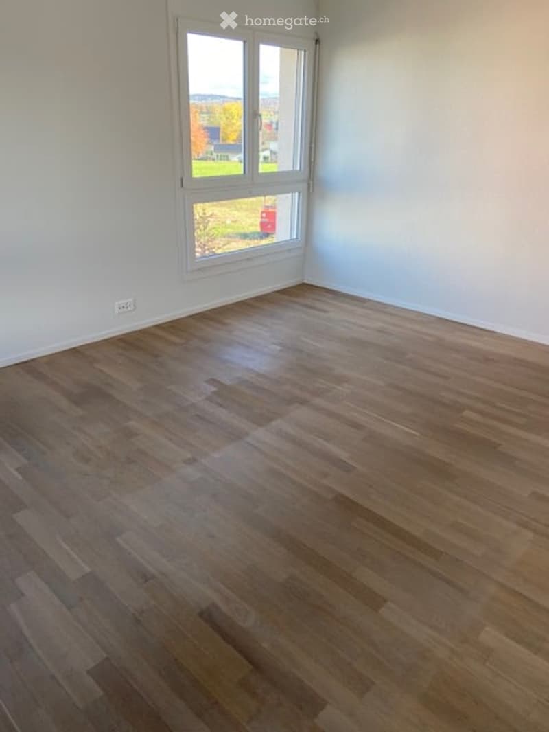 Empty room with wooden flooring and large window showing outdoor view. No furniture or equipment present.