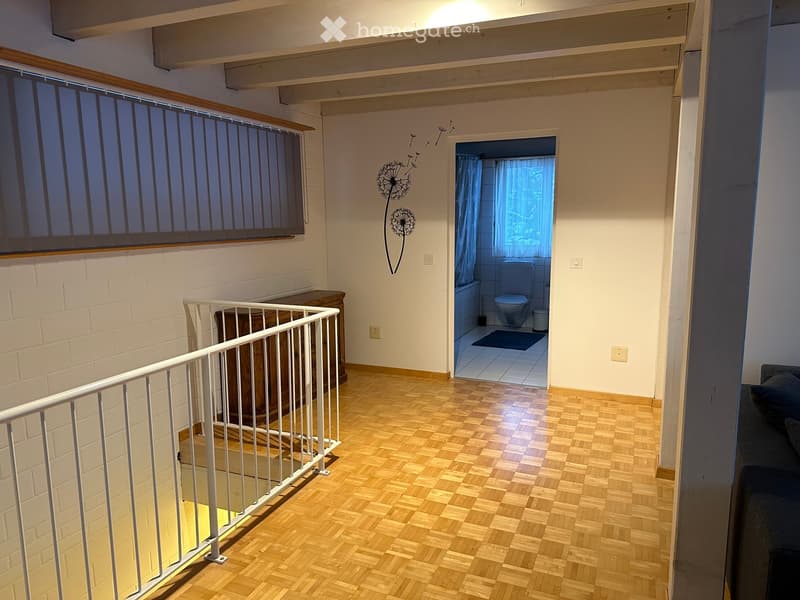 Hallway with wooden flooring, white railing, and a view into a small bathroom with a toilet and bathtub.