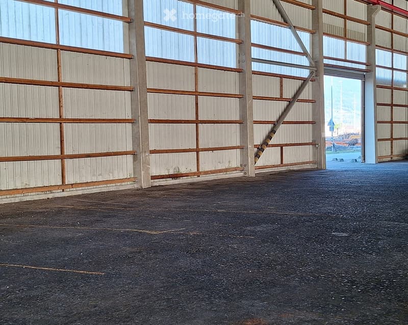 Empty warehouse space with concrete floor, metal walls, and wooden beams. No furniture or equipment present.