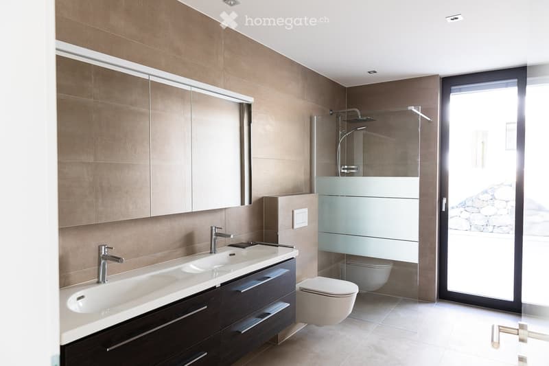 Modern bathroom with double sink, mirrored cabinet, toilet, and glass-enclosed shower area.