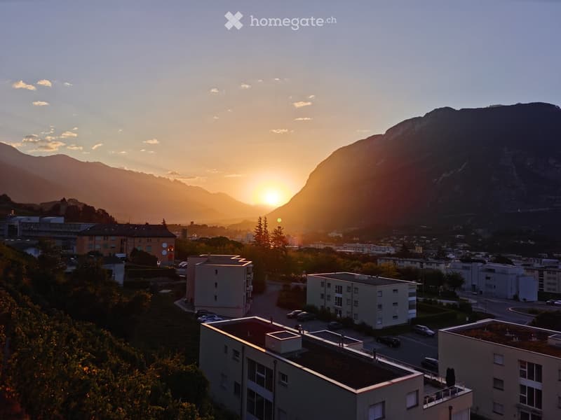 A panoramic view of a town with buildings, roads, and mountains during sunset.