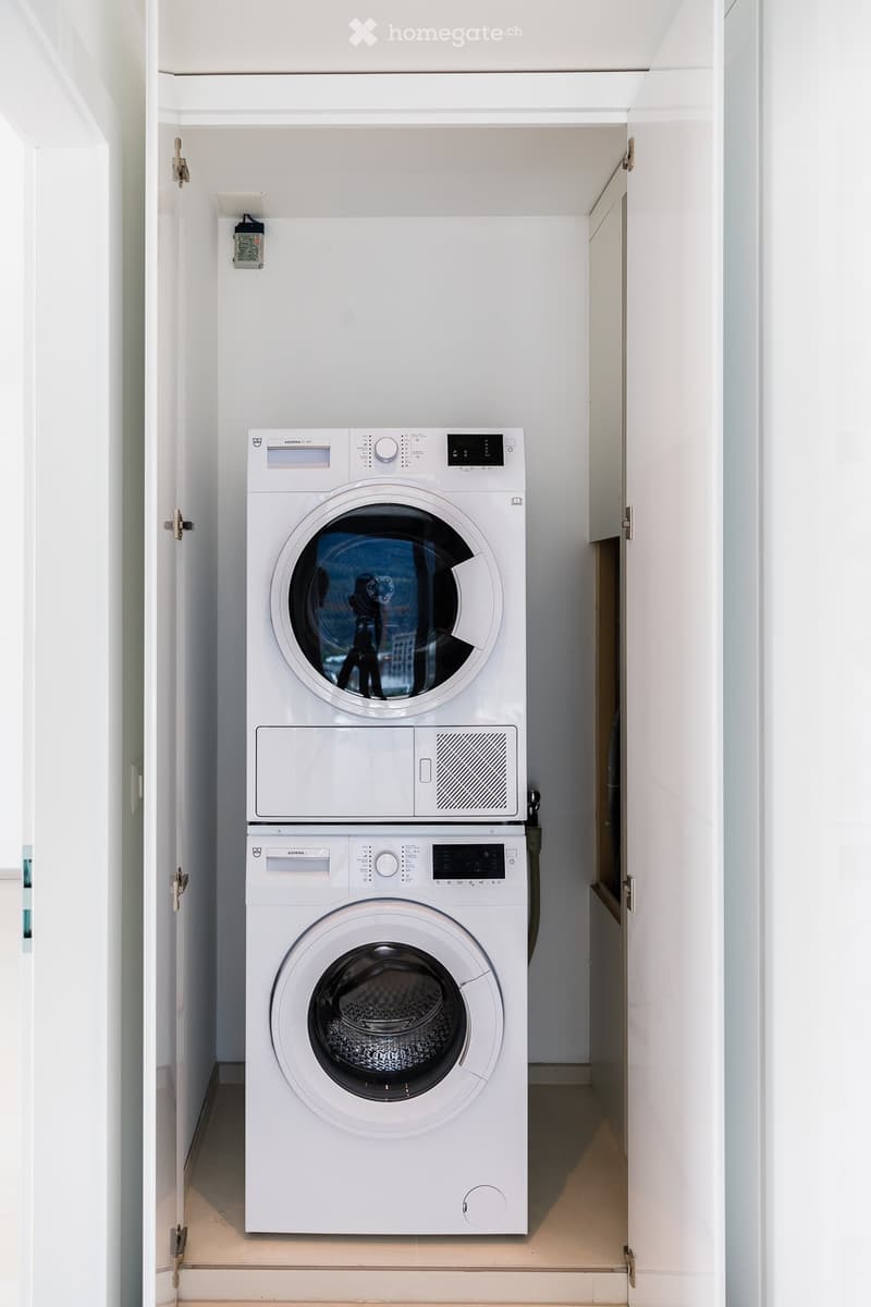 A compact bathroom with a stacked washing machine and dryer unit, white walls, and light-colored flooring.